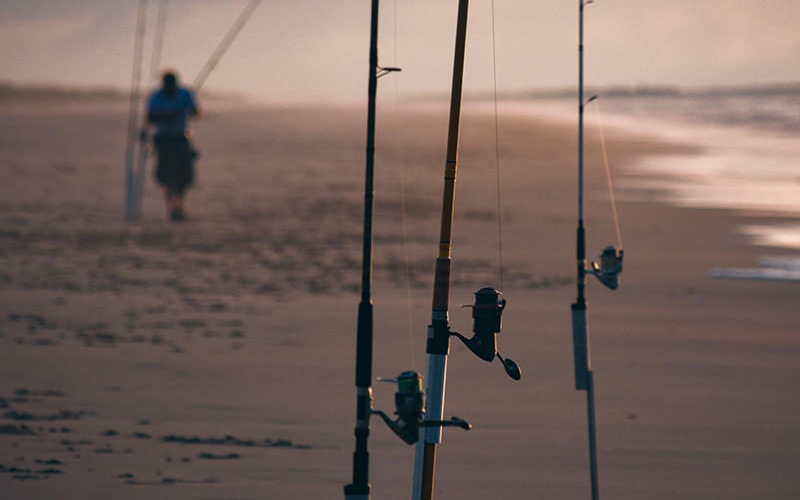 fishing poles in the sand at the beach and man standing with a pole in the background