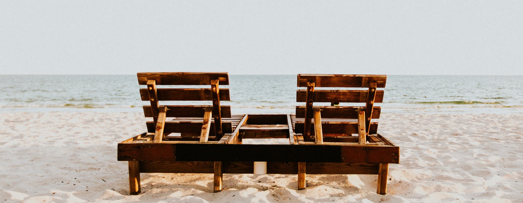 wood framed beach chairs on the shore looking toward the ocean