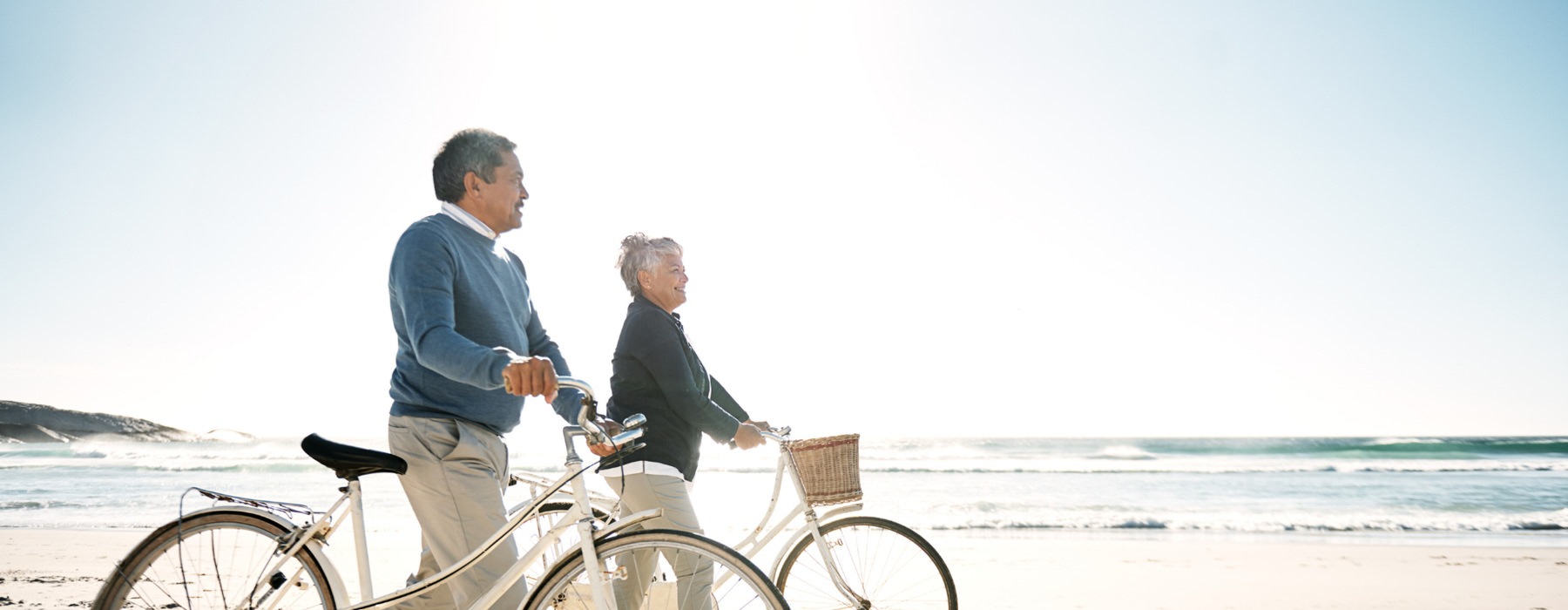 Lifestyle photo of couple walk their bicycles along the beach