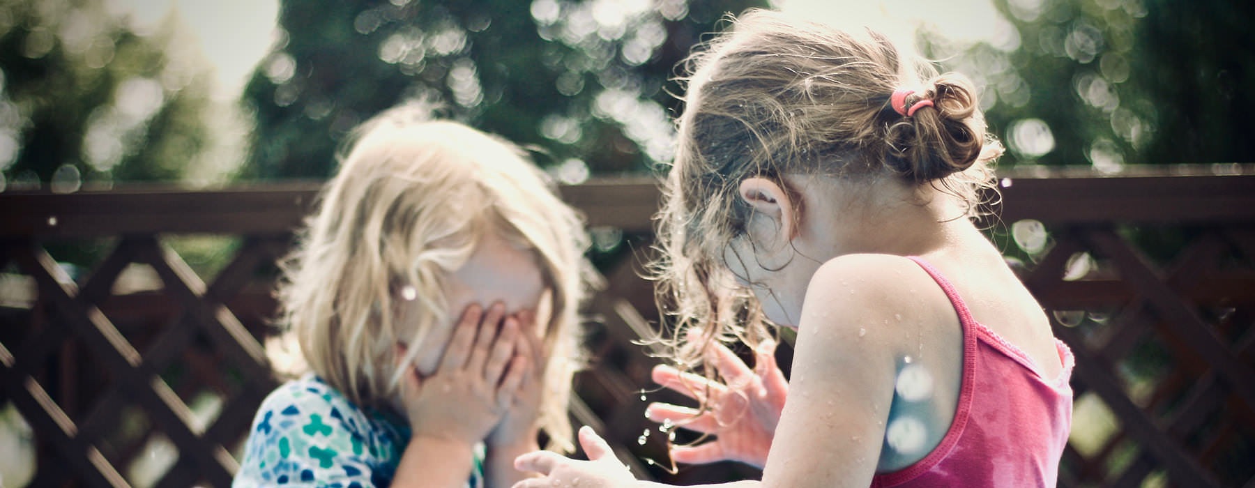 two little girls hide their faces as they play outside